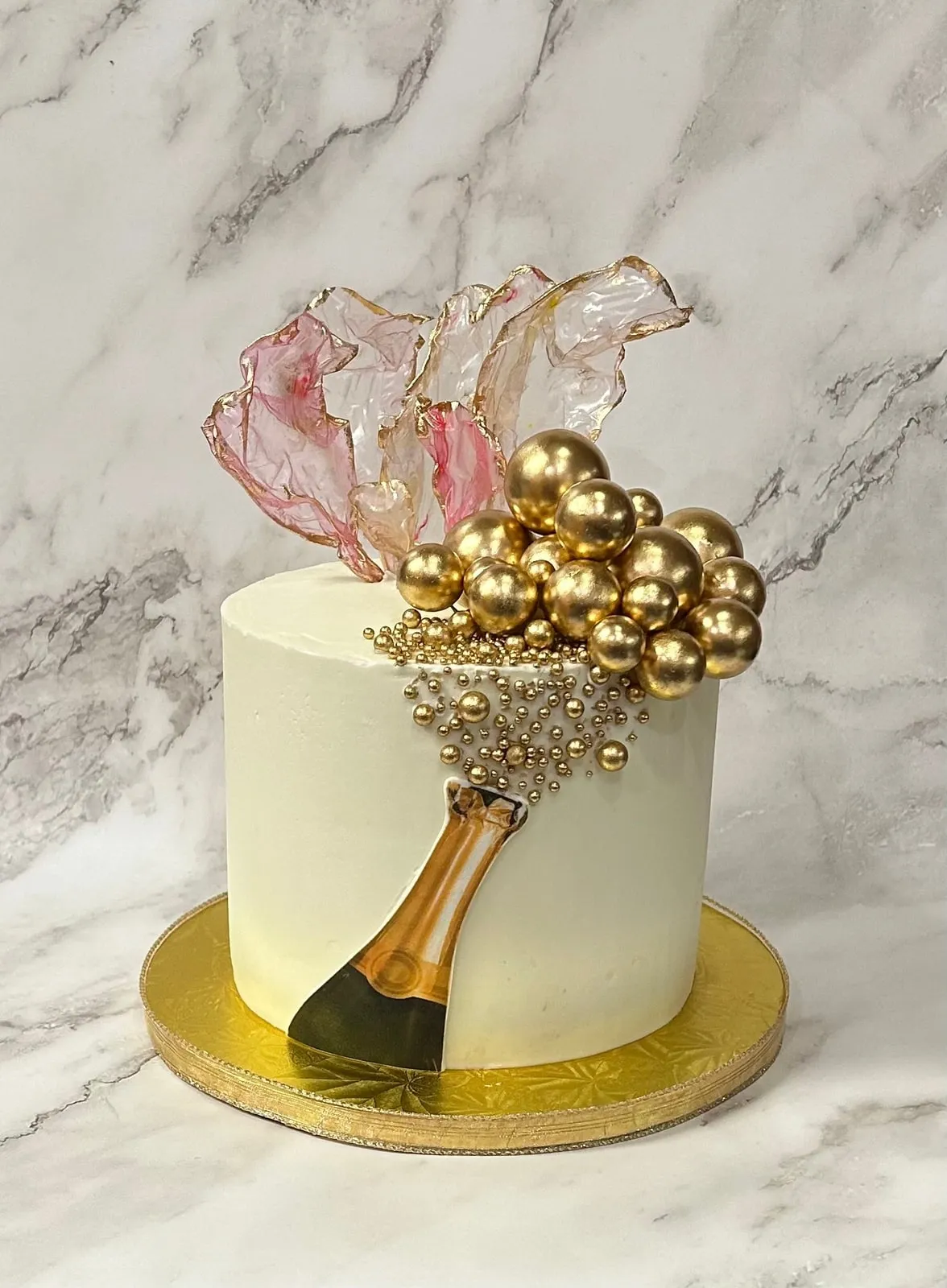 Ivory and gold celebration cake with a blush isomalt sail and gold spheres