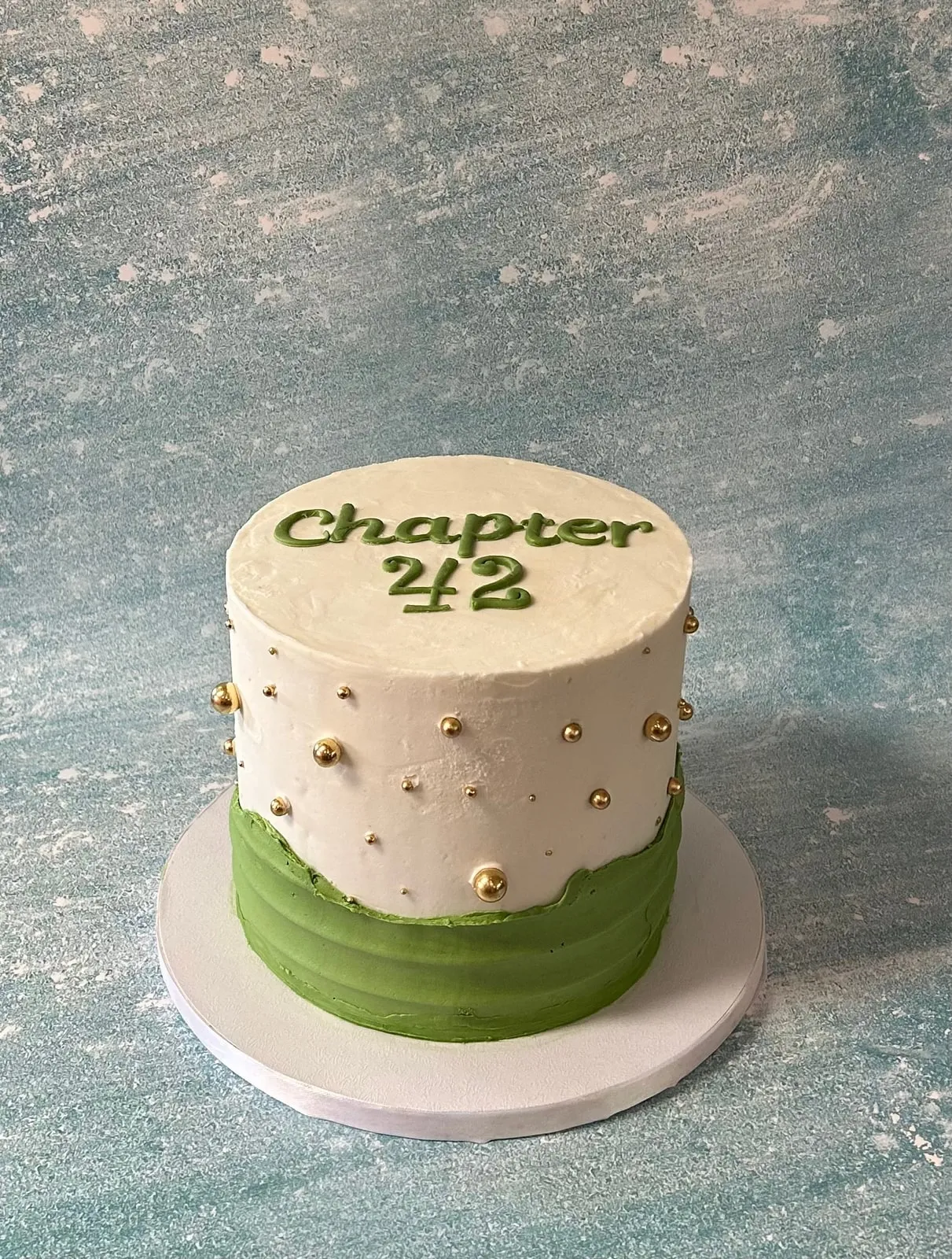 Minimal cream and sage birthday cake with gold dragees and a Chapter 42 plaque