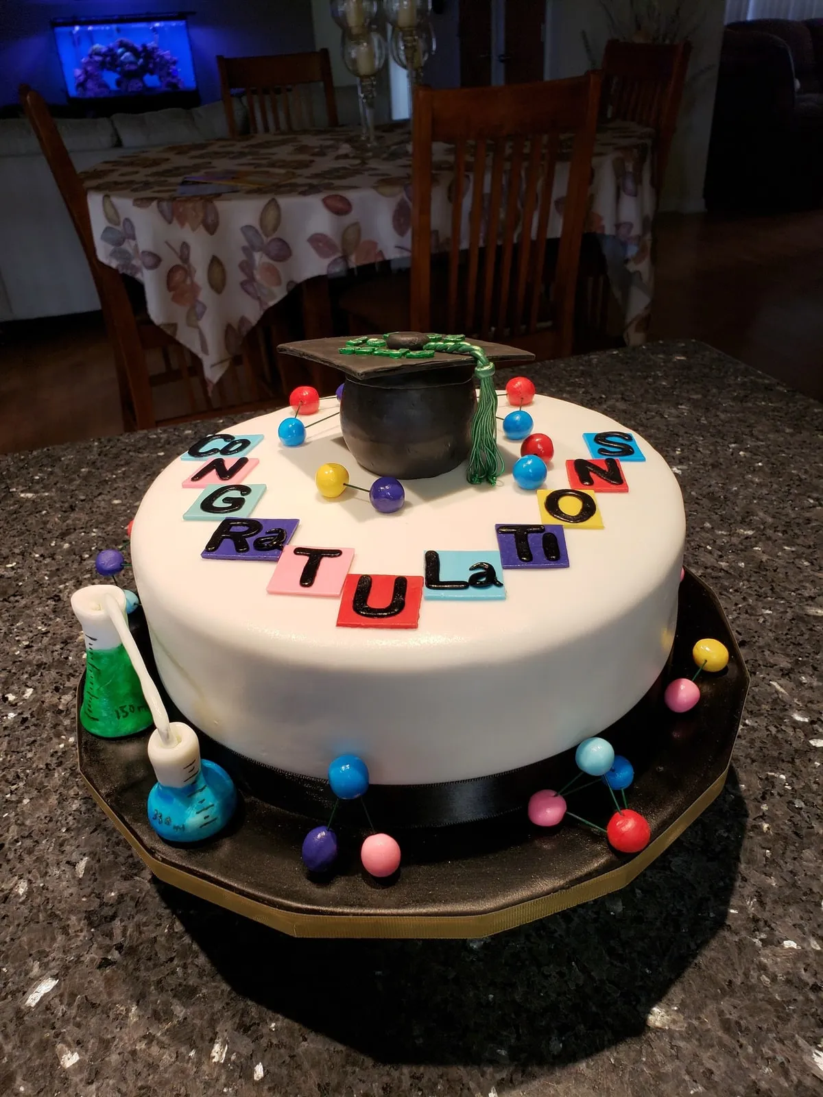 White graduation cake with fondant letters, a mortarboard and confetti dots