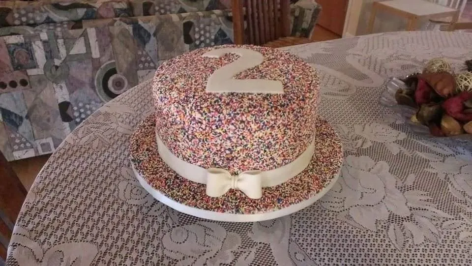 Ivory second birthday cake covered in rainbow sprinkles with a fondant bow