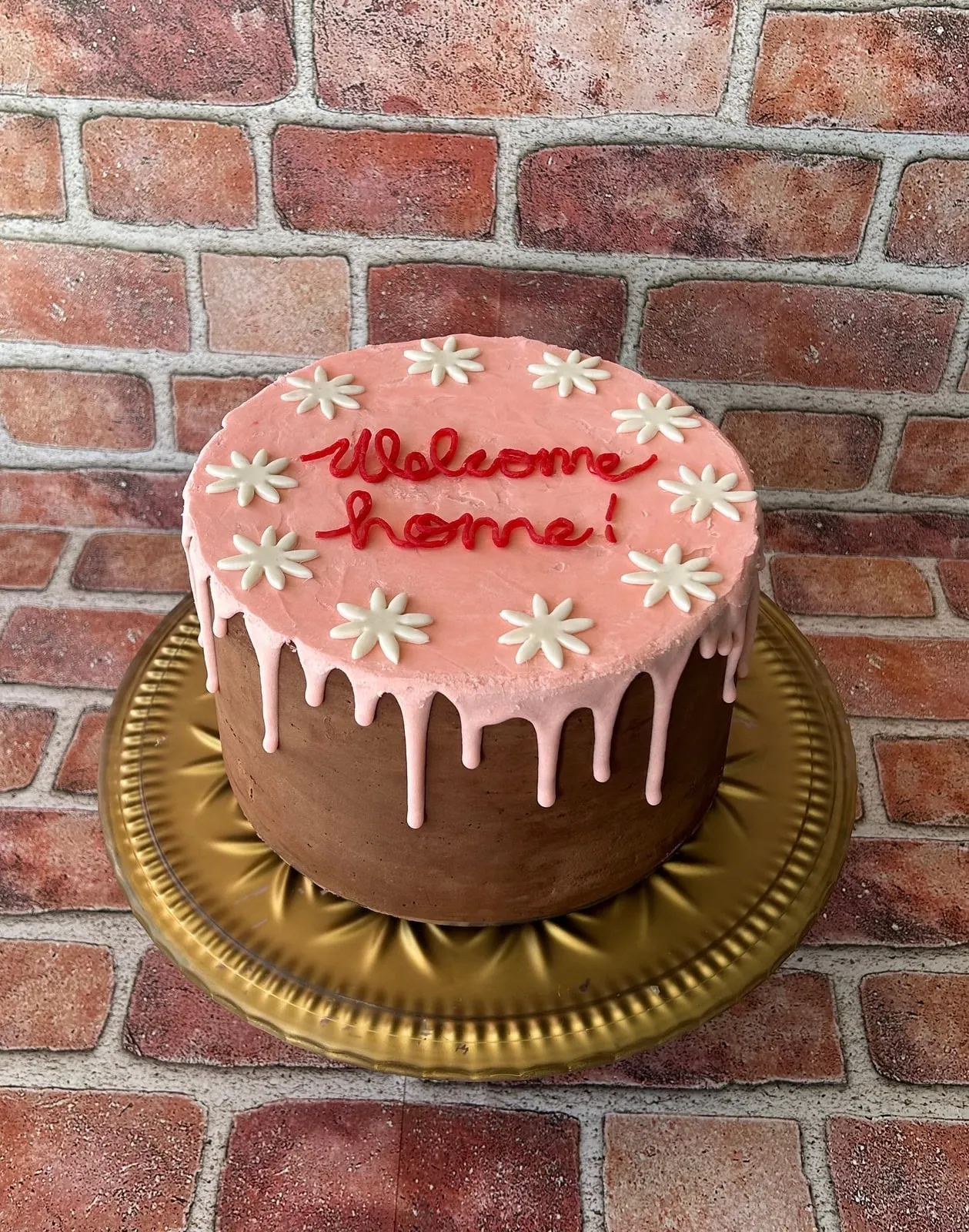 Welcome Home cake with chocolate drip over pink buttercream and piped daisies
